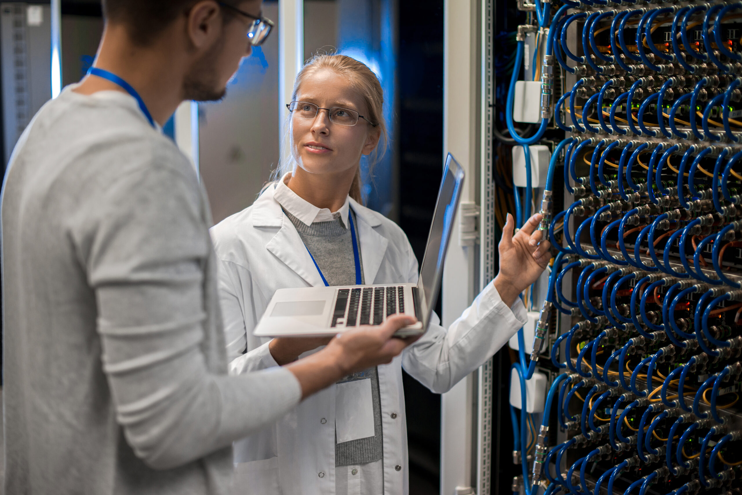 Portrait of young man and woman standing by server cabinets and discussing data while working with supercomputer in science center